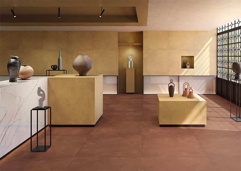 Keope Plate Copper | Hall di un museo: le pareti e gli espositori sono rivestiti con Brass, nel formato120x120. A pavimento Copper, nel formato 120x120. Il bancone è rivestito con le grandi lastre Calacatta Statuarietto 120x278 della serie effetto marmo Elements Lux.